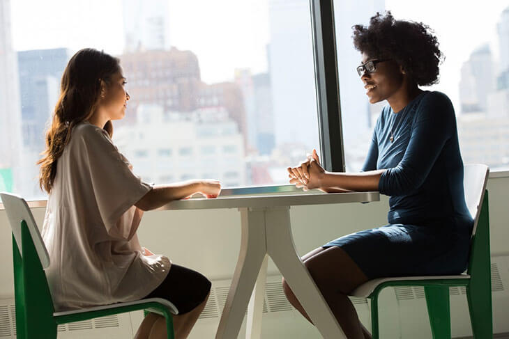 Two People Sat Talking At A Table about the Confidence Gap